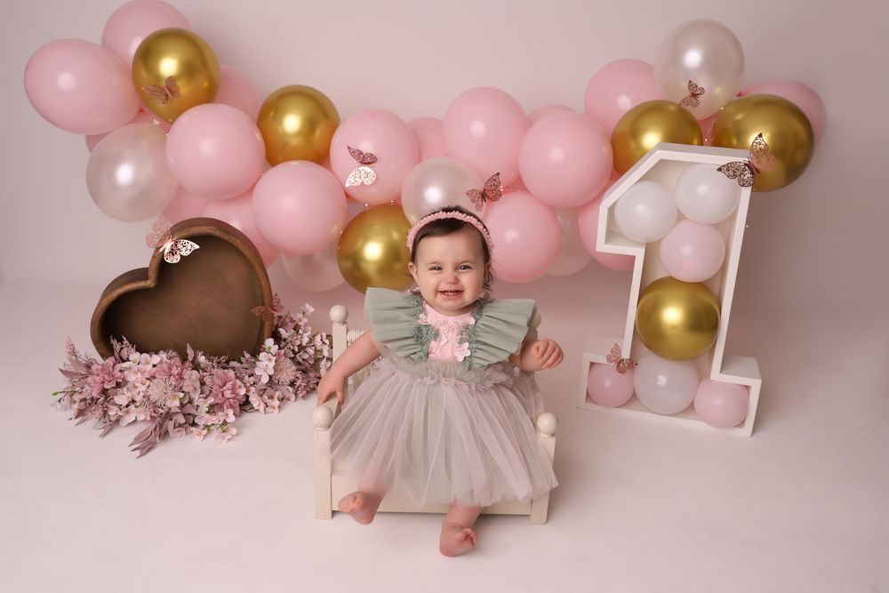 First birthday photo setup with pink and gold balloons and floral decorations.