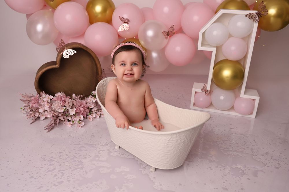 Birthday photo session featuring white bathtub prop and pink balloon decorations.