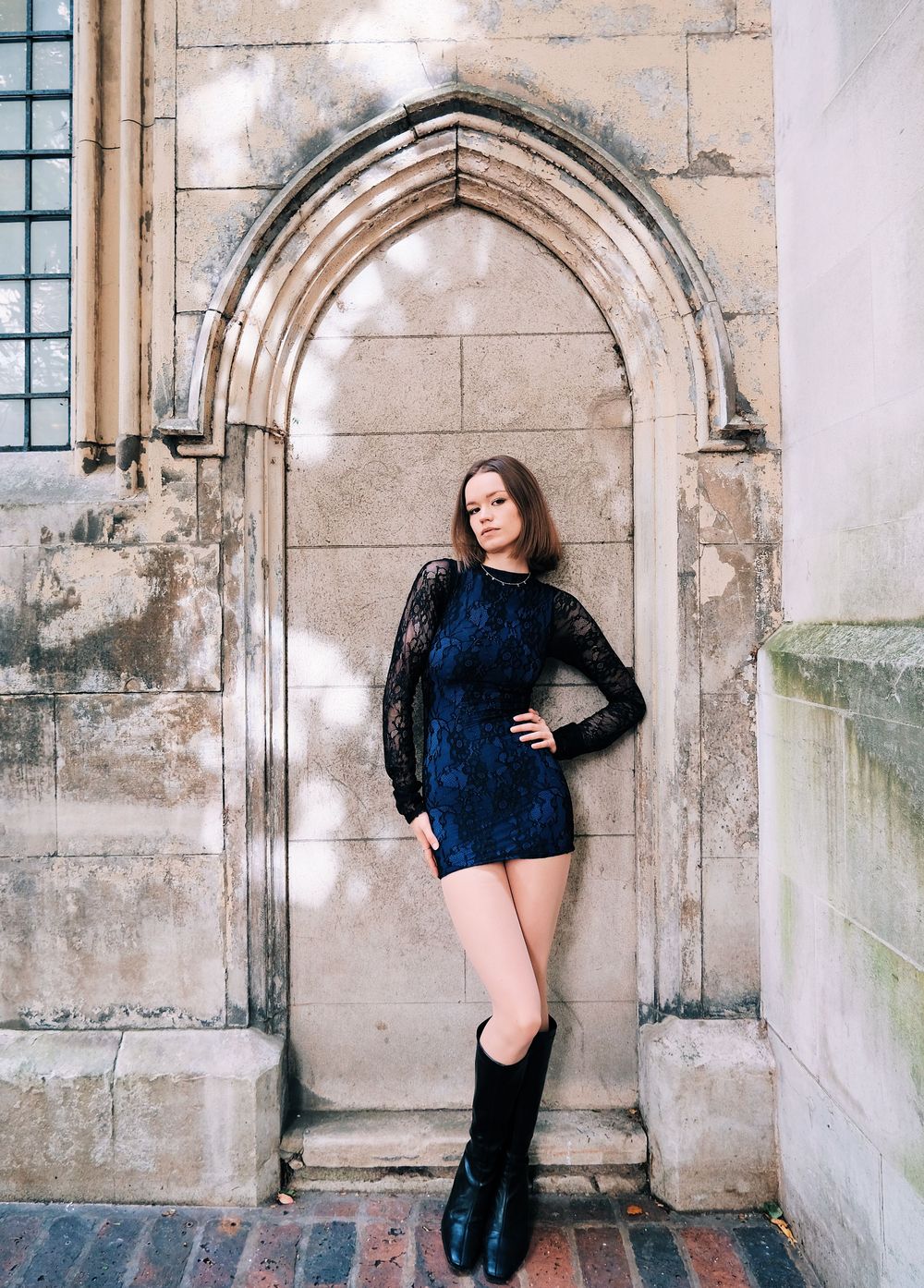 A series of fashion poses against a stone archway wall showing different angles in a black outfit and boots.