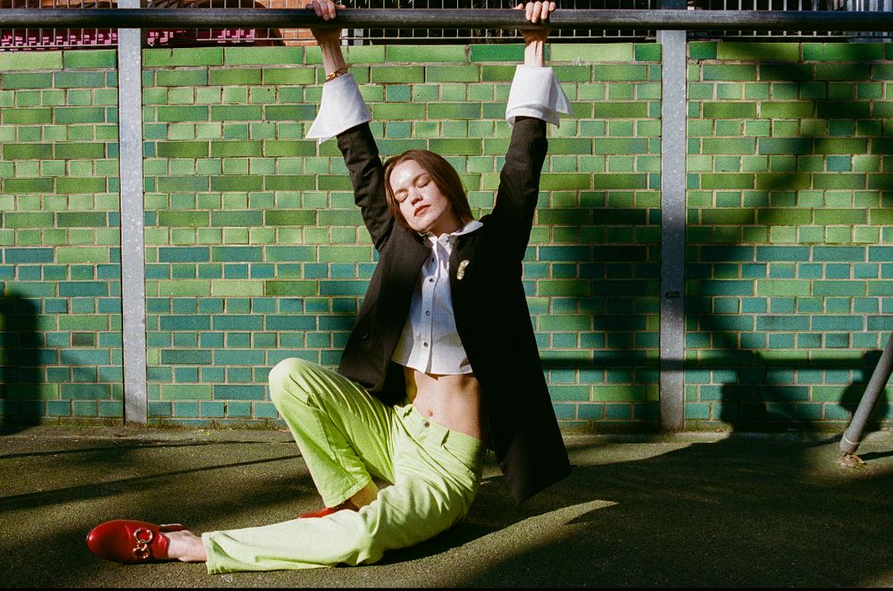 Three action shots show a person in green performing acrobatic dance moves on a city street against a brick wall background.