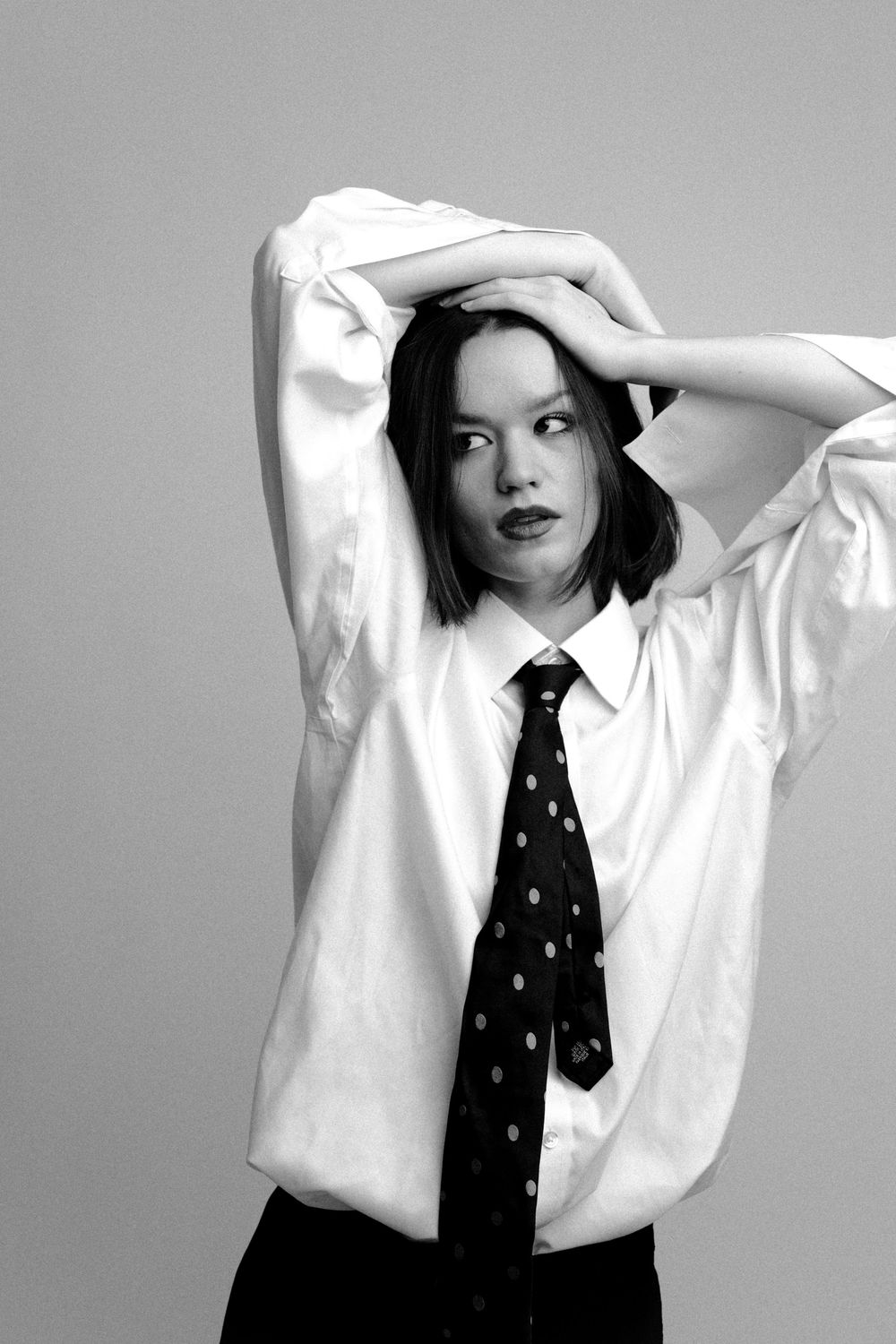 A series of black and white fashion photographs showing a model in a white shirt and polka dot tie striking different poses.
