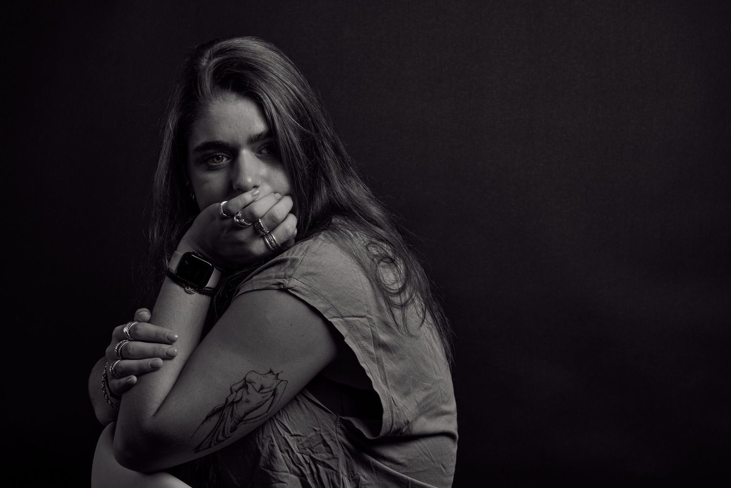 Zwart wit portret van een jonge vrouw met sieraden en tatoeages.