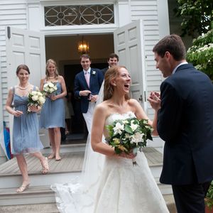 Wedding party celebrates on a white porch with bridesmaids in blue dresses and the bride in a flowing white gown.