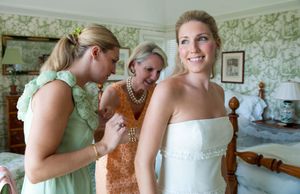 A wedding party gets ready in a room with green floral wallpaper as they help with final preparations.
