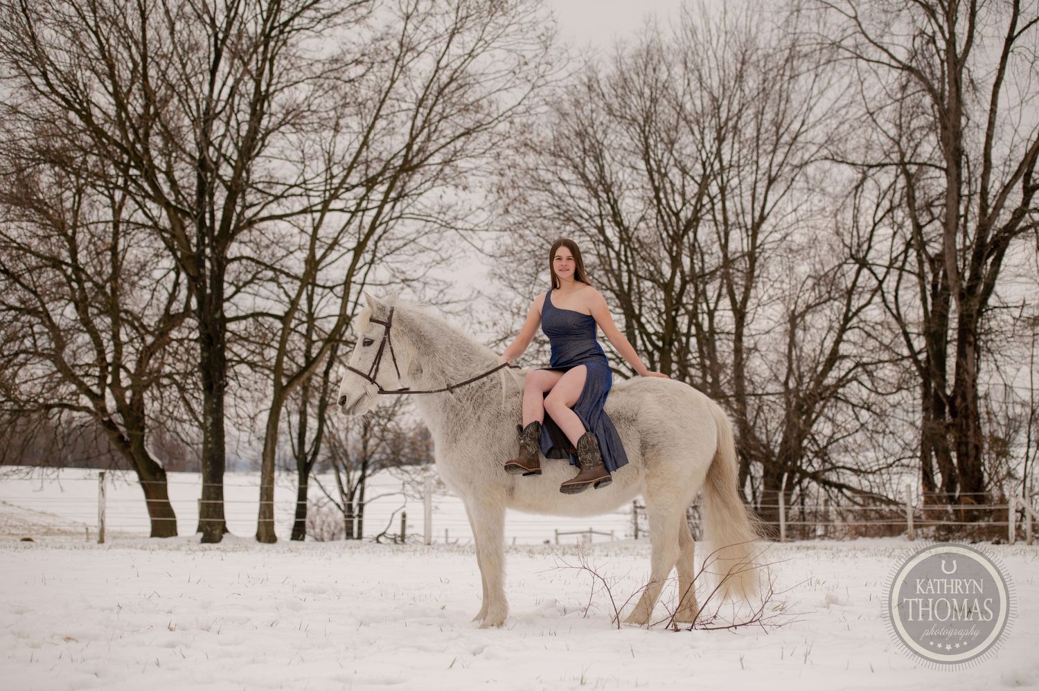 A white horse and rider in a snowy landscape surrounded by bare winter trees.