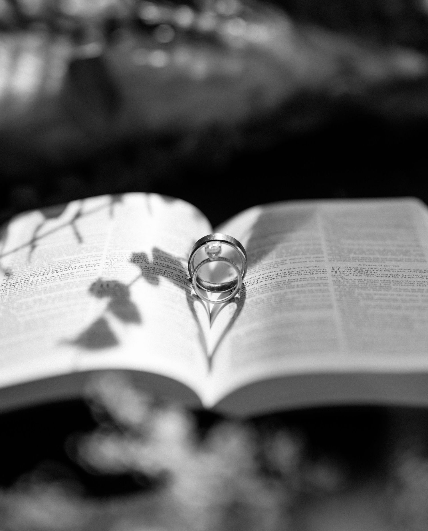 Wedding ring casting heart shadow on open book pages in black and white.