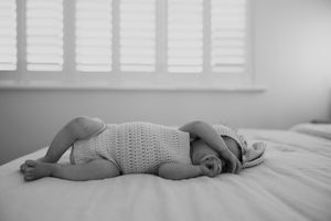 Black and white photo of a sleeping baby curled up peacefully on soft bedding.