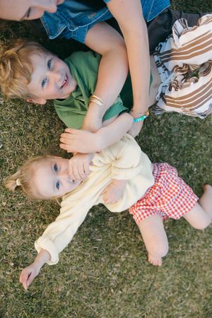 Two children lie together on grass during a playful outdoor moment on a sunny day.
