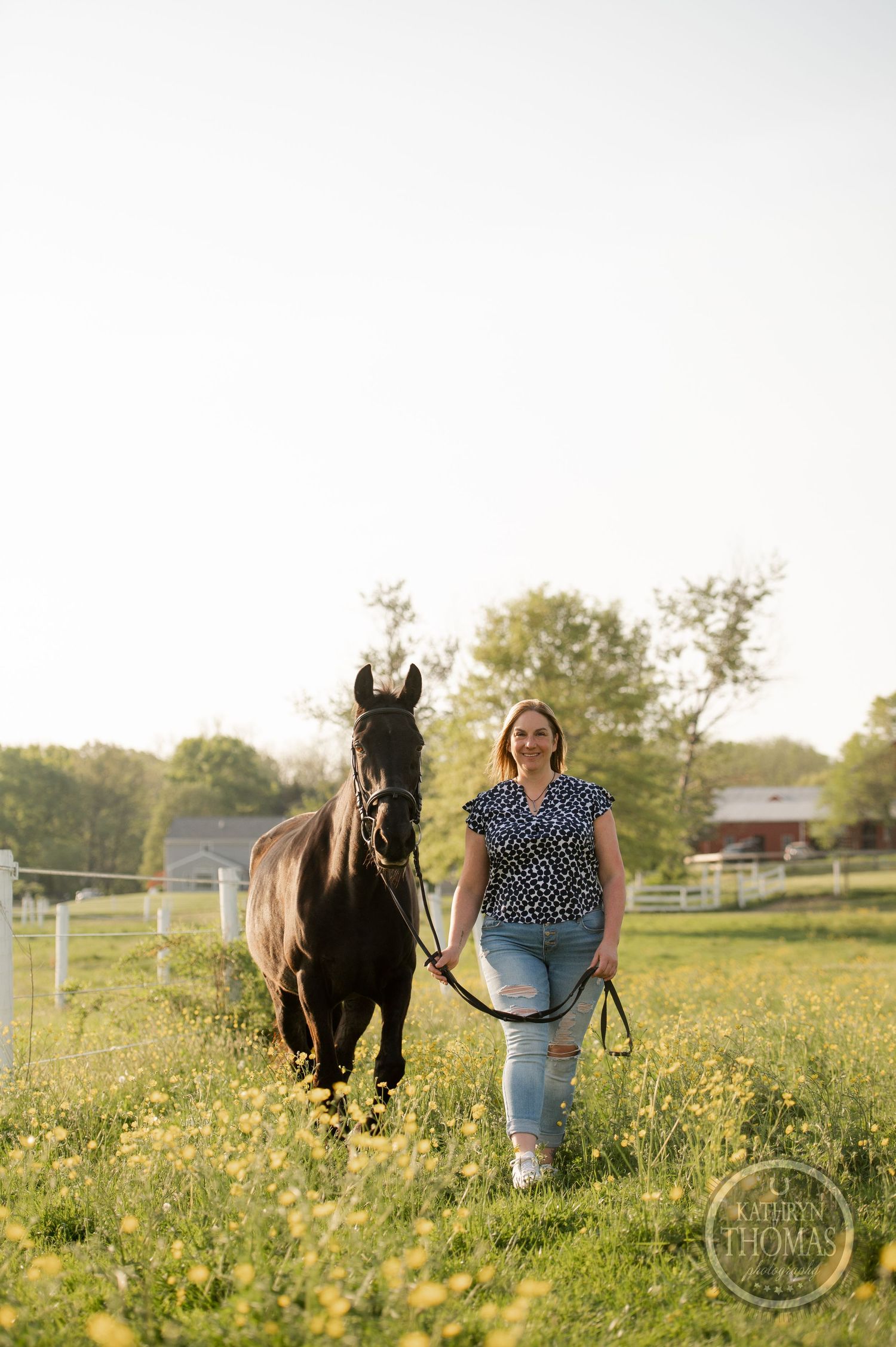 A dark horse walks alongside its companion through a wildflower-filled pasture at golden hour.