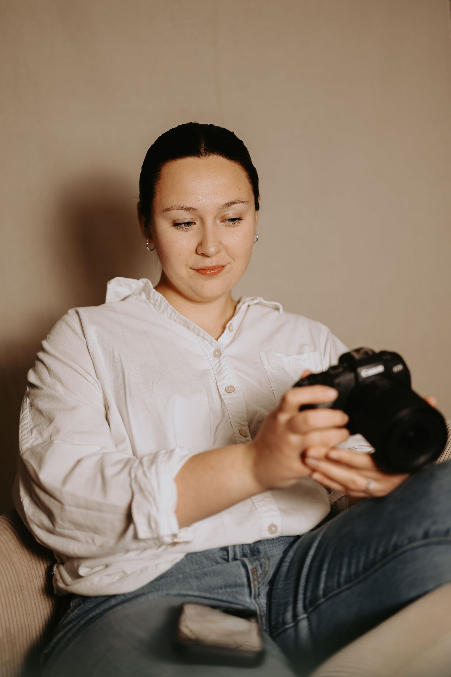 Photographer poses with camera against blurred nature background in casual attire.