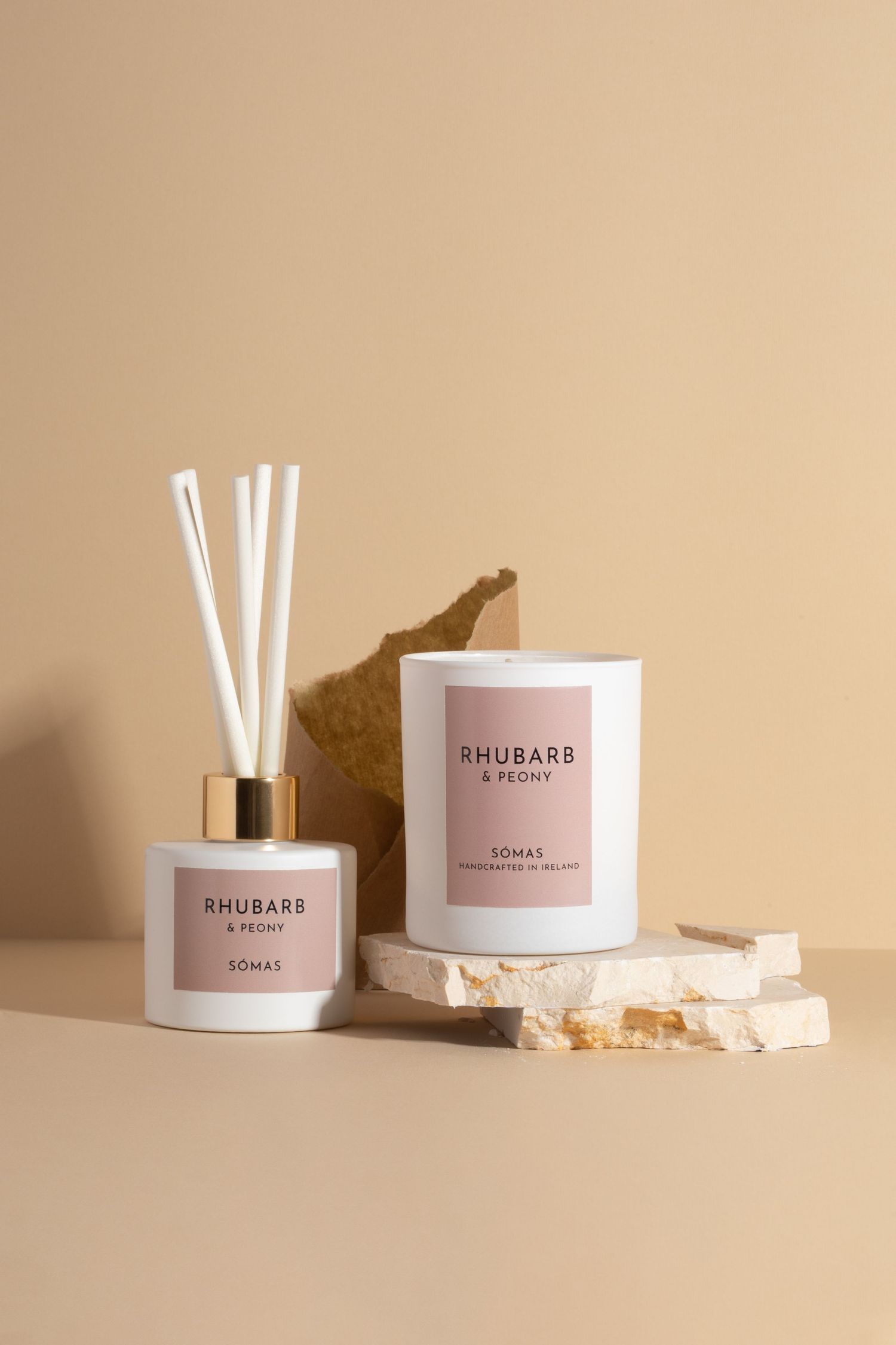 Rhubarb & Peony home fragrance set with reed diffuser and candle on textured stone surface. There is textured paper to add interest.