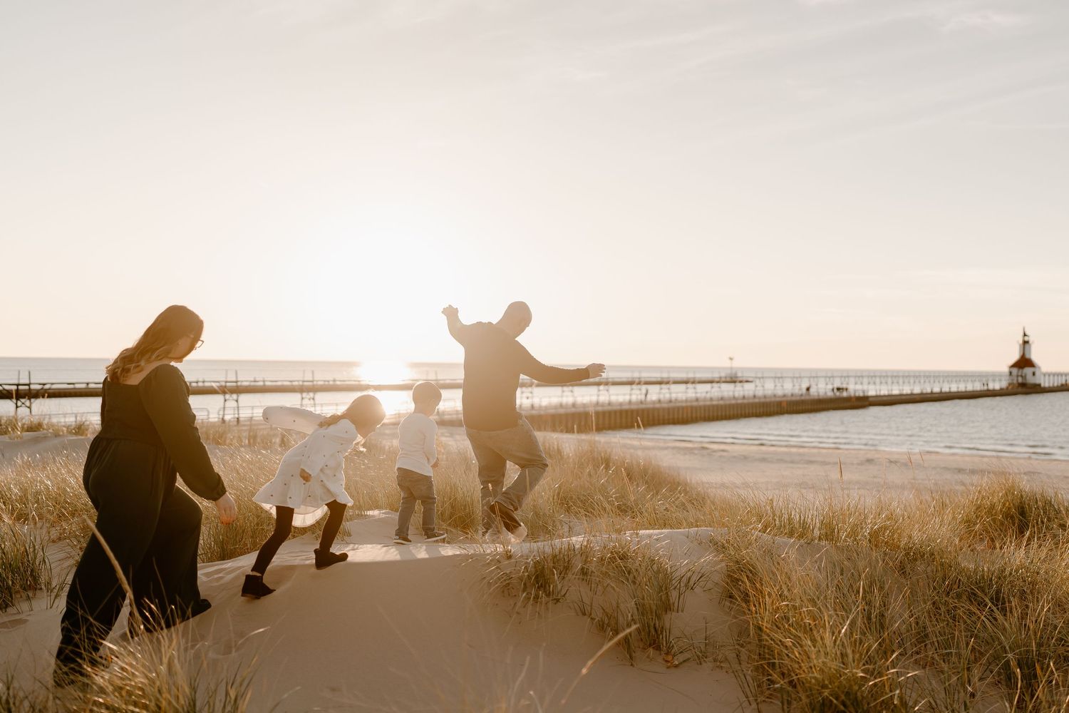 Silhouettes of people jumping and posing on a beach path at sunset with a lighthouse in the background.