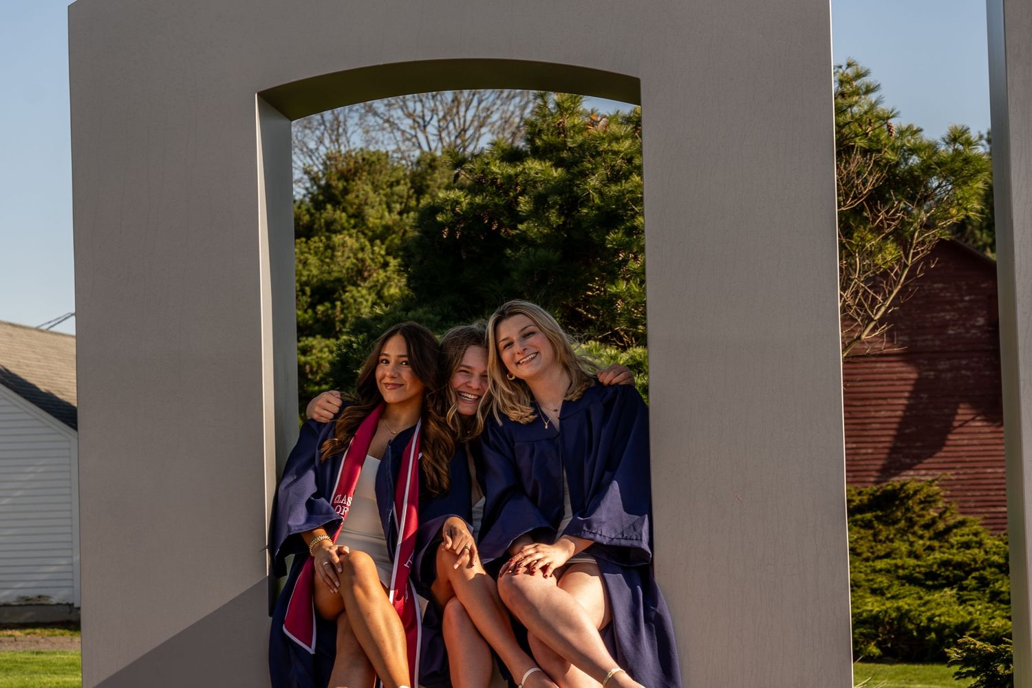 Three girls in graduation gowns smiling and celebrating outdoors after graduation ceremony