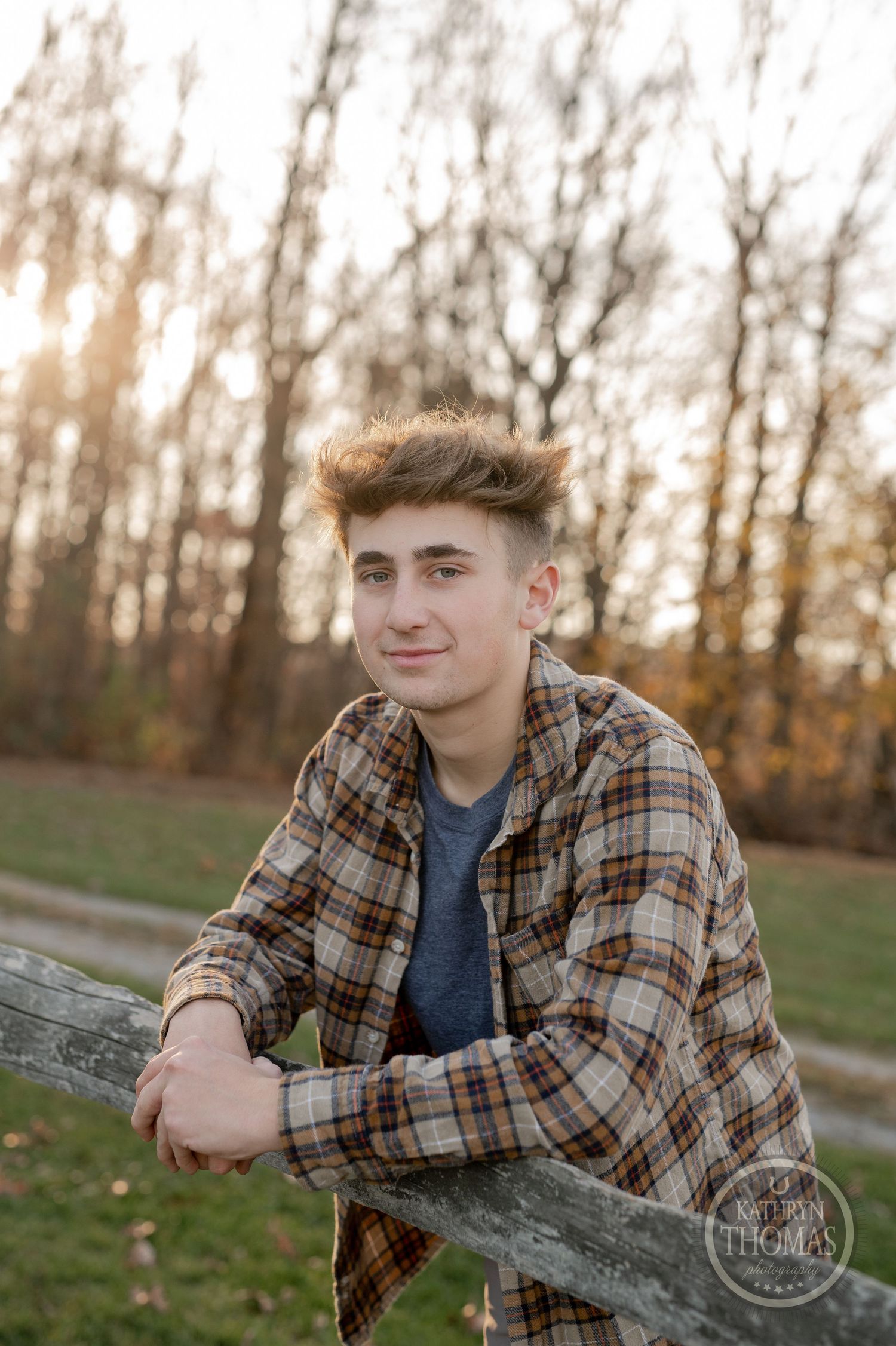 A casual outdoor portrait of someone in plaid leaning on a wooden fence at sunset.