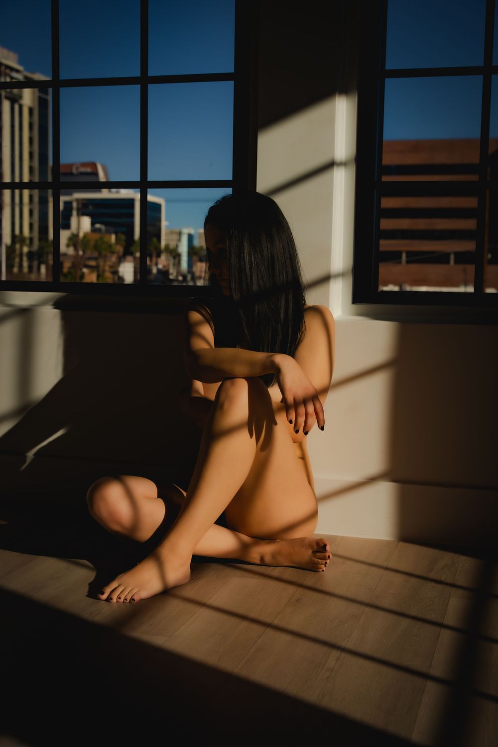 Artistic boudoir image of a nude woman in front of a window with the city of Las Vegas in the background and dramatic lighting flowing in.