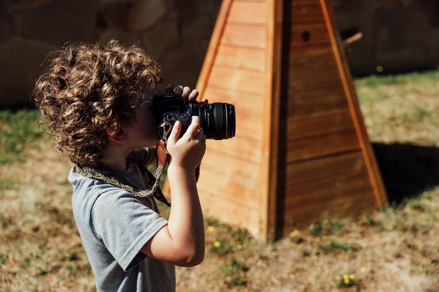 Photographer using DSLR camera outdoors with wooden structure in background.