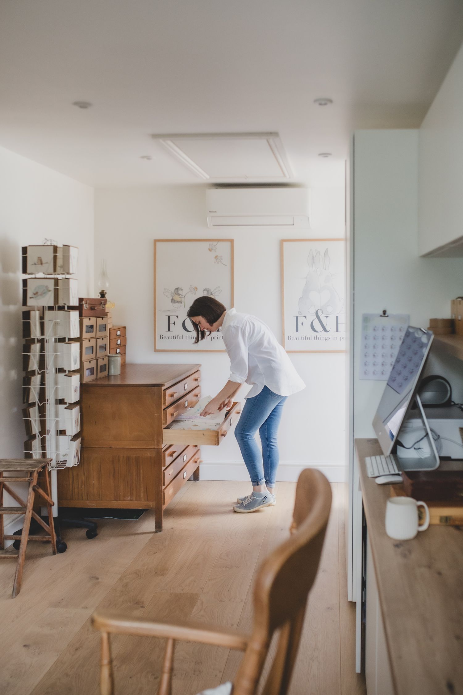Someone organizing items in a modern minimalist home office with wooden furniture and framed artwork. Small Business storytelling photos