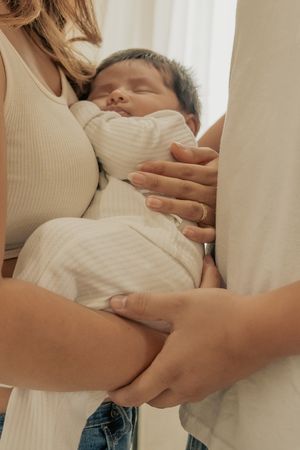 Peaceful sleeping newborn in white clothing held by loving parents.
