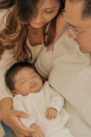 Parents lovingly gazing at their sleeping newborn baby dressed in white.
