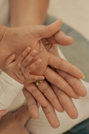 Close-up of tiny baby hand held in parent's palm showing tender touch.
