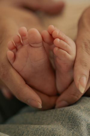 Tiny newborn feet cradled gently in adult hands against denim background.