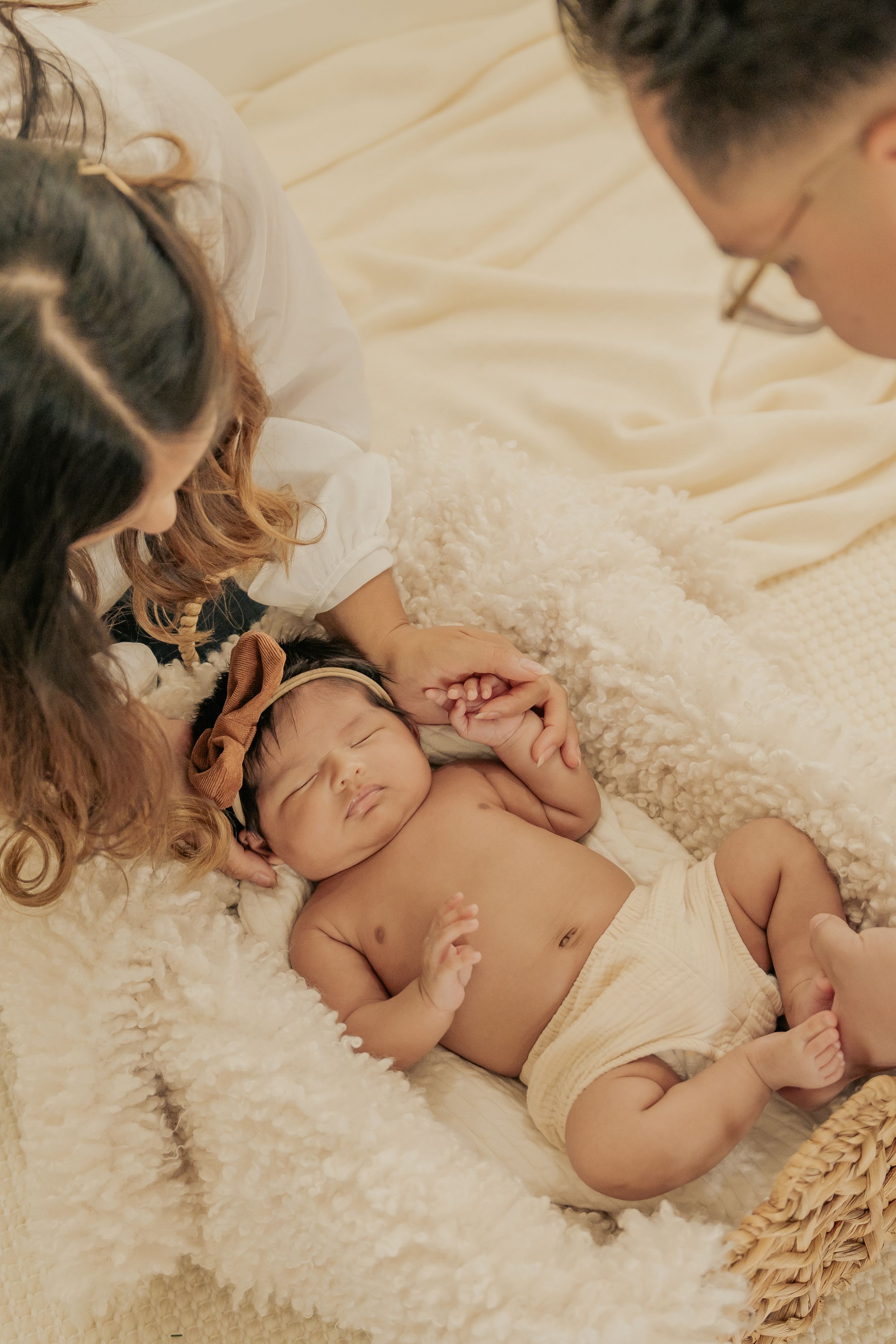 Peaceful sleeping infant in diaper rests on soft white blanket beside parents.