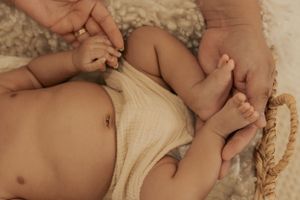 Close-up of baby's body in white diaper with adult hands tenderly touching.