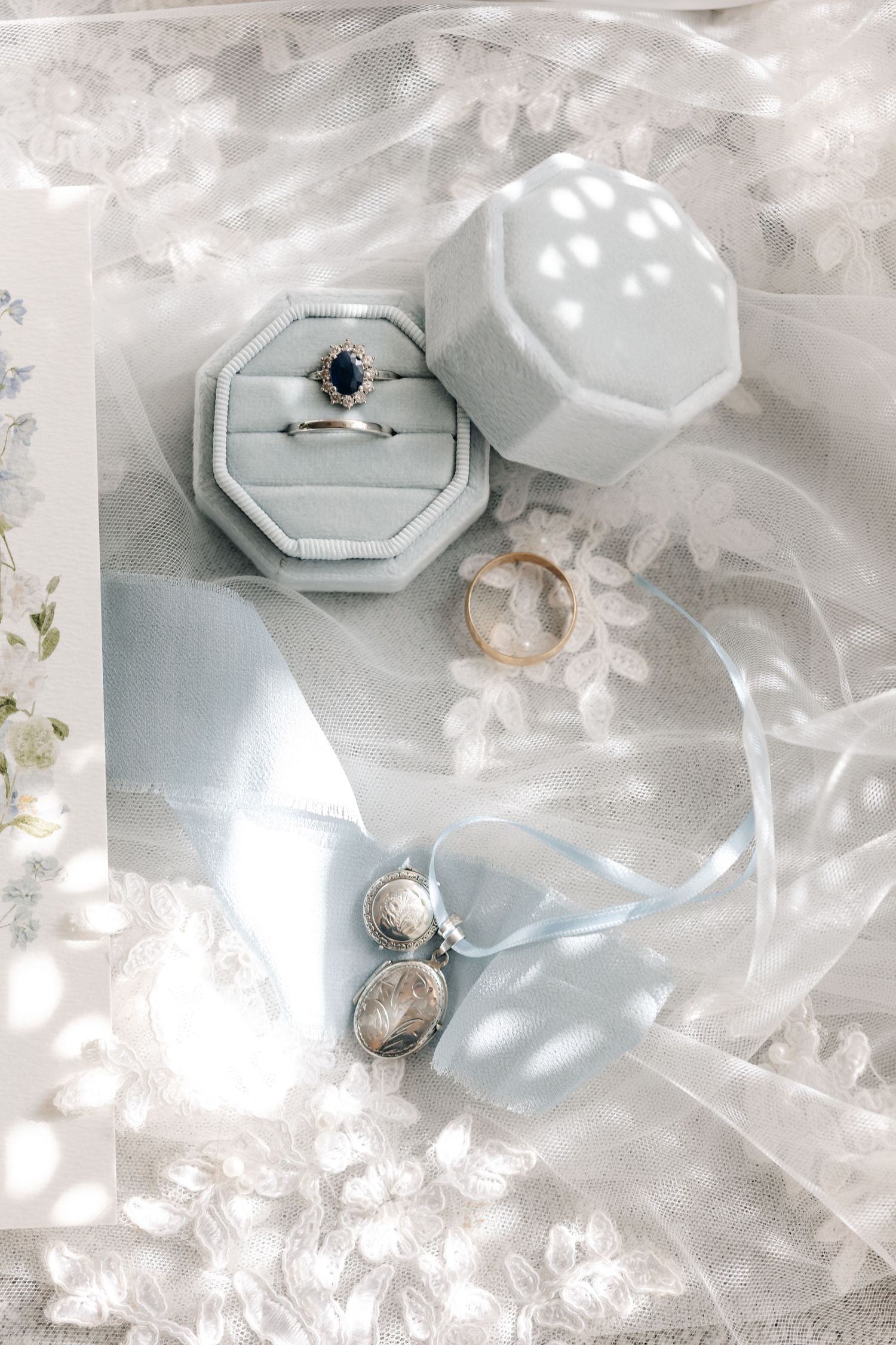 Elegant engagement rings and wedding bands displayed on light gray surfaces with soft white fabric and delicate lighting.