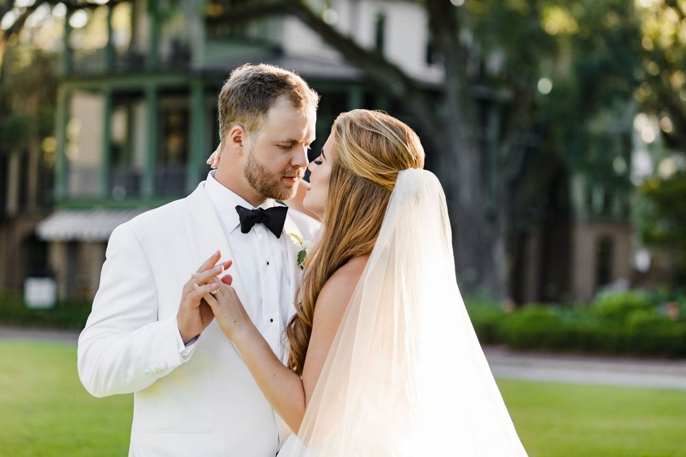 Bride and groom share a romantic dance outdoors, with the groom in a white tuxedo and bride in a flowing veil.