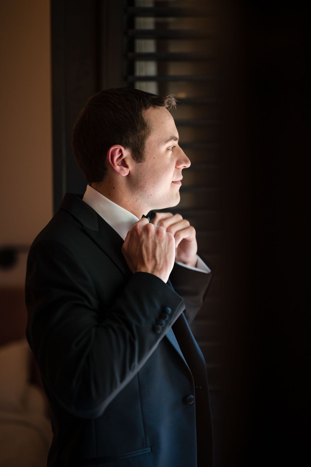 Groom adjusting bow tie near window during wedding day at Hotel El Convento Puerto Rico