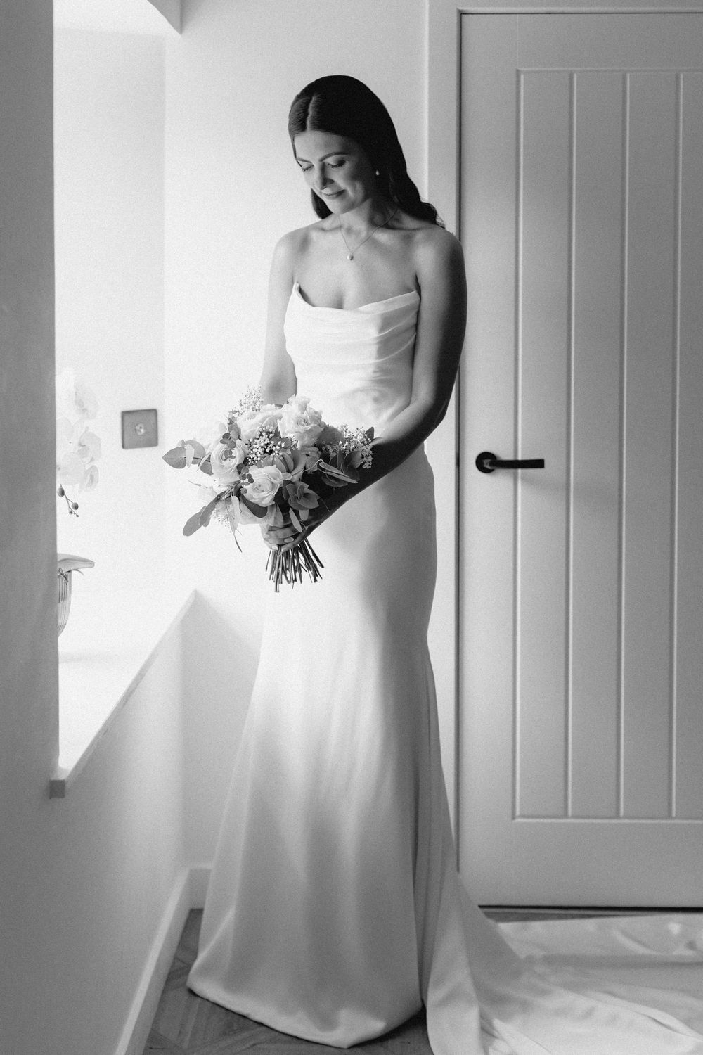 A series of black and white bridal portraits showing a wedding dress in different elegant poses against a white wall.