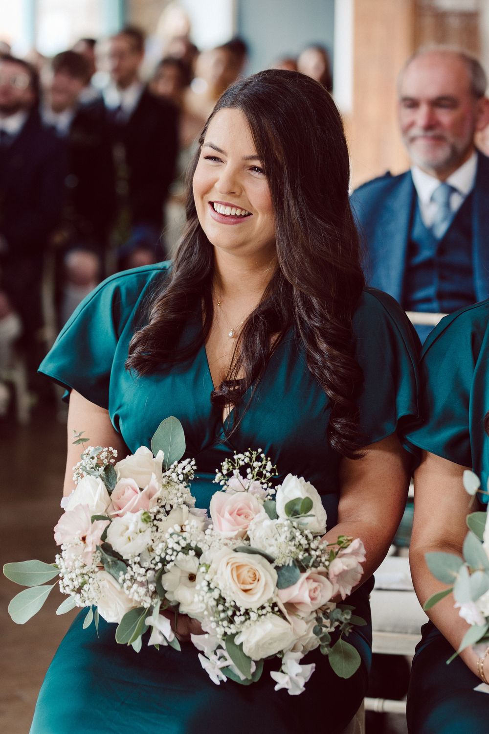 Bridesmaid in emerald green dress holds elegant white and blush pink floral bouquet with eucalyptus accents.