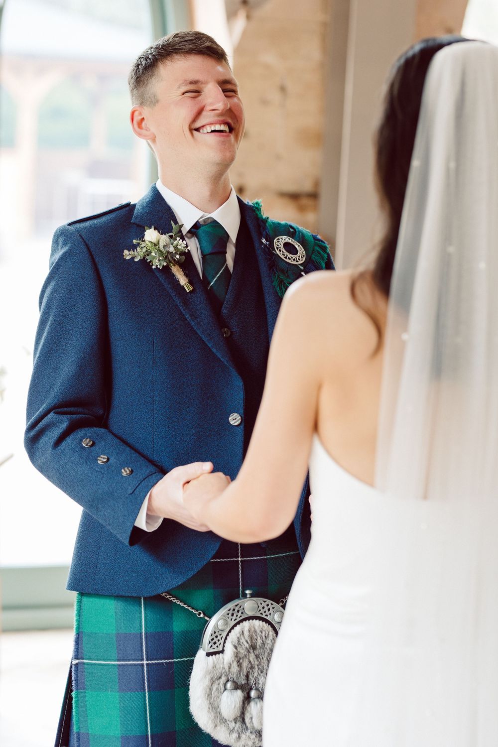 First look photos show a joyful moment between newlyweds, with the groom wearing a traditional Scottish kilt and navy jacket.