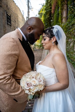 A romantic wedding couple shares tender moments in front of an ivy-covered brick wall.