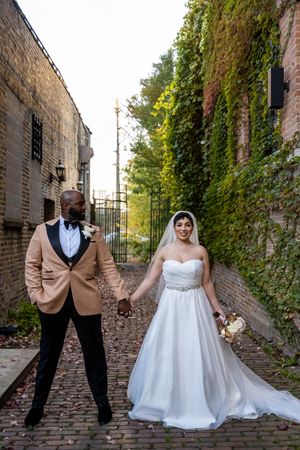 A couple poses for wedding photos in a charming brick alley with ivy-covered walls and cobblestone ground.