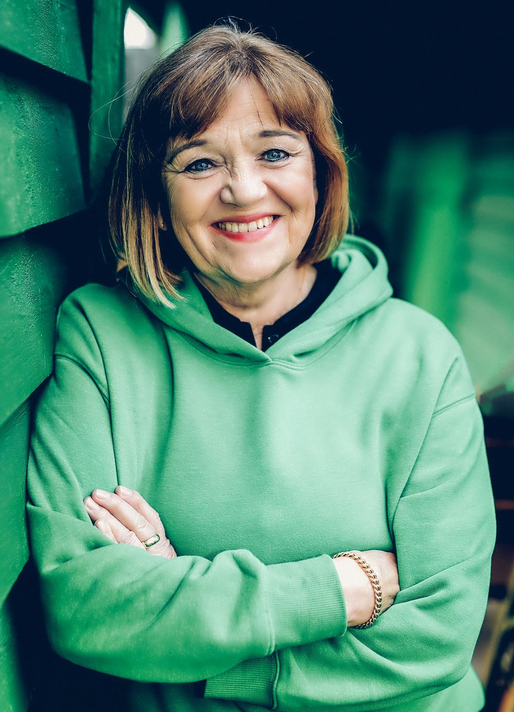 A person in a mint green hoodie smiles warmly while posing against a blurred green background.