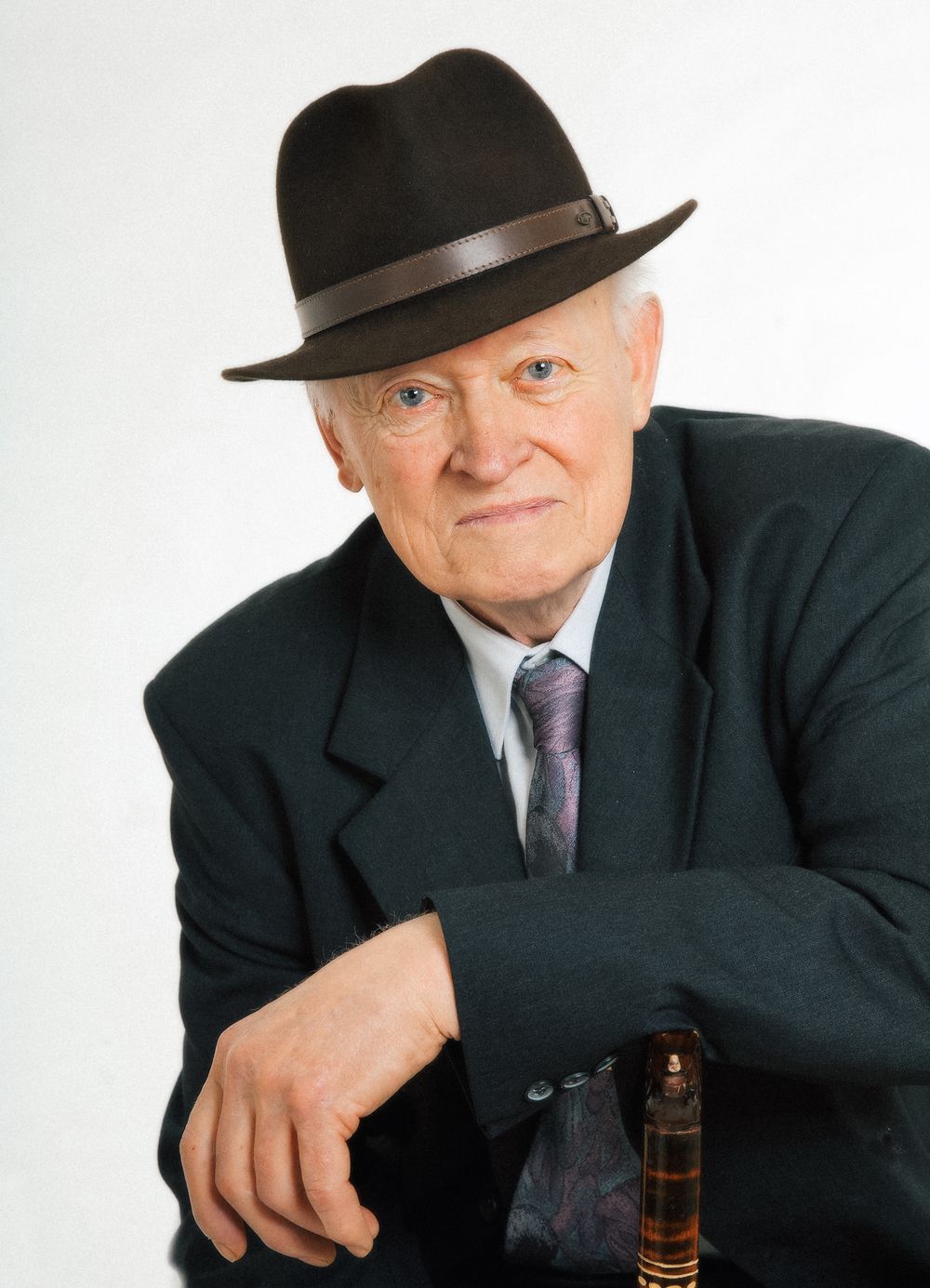 A person in a black hat and suit poses with a bottle in a series of expressive portrait shots against white background.
