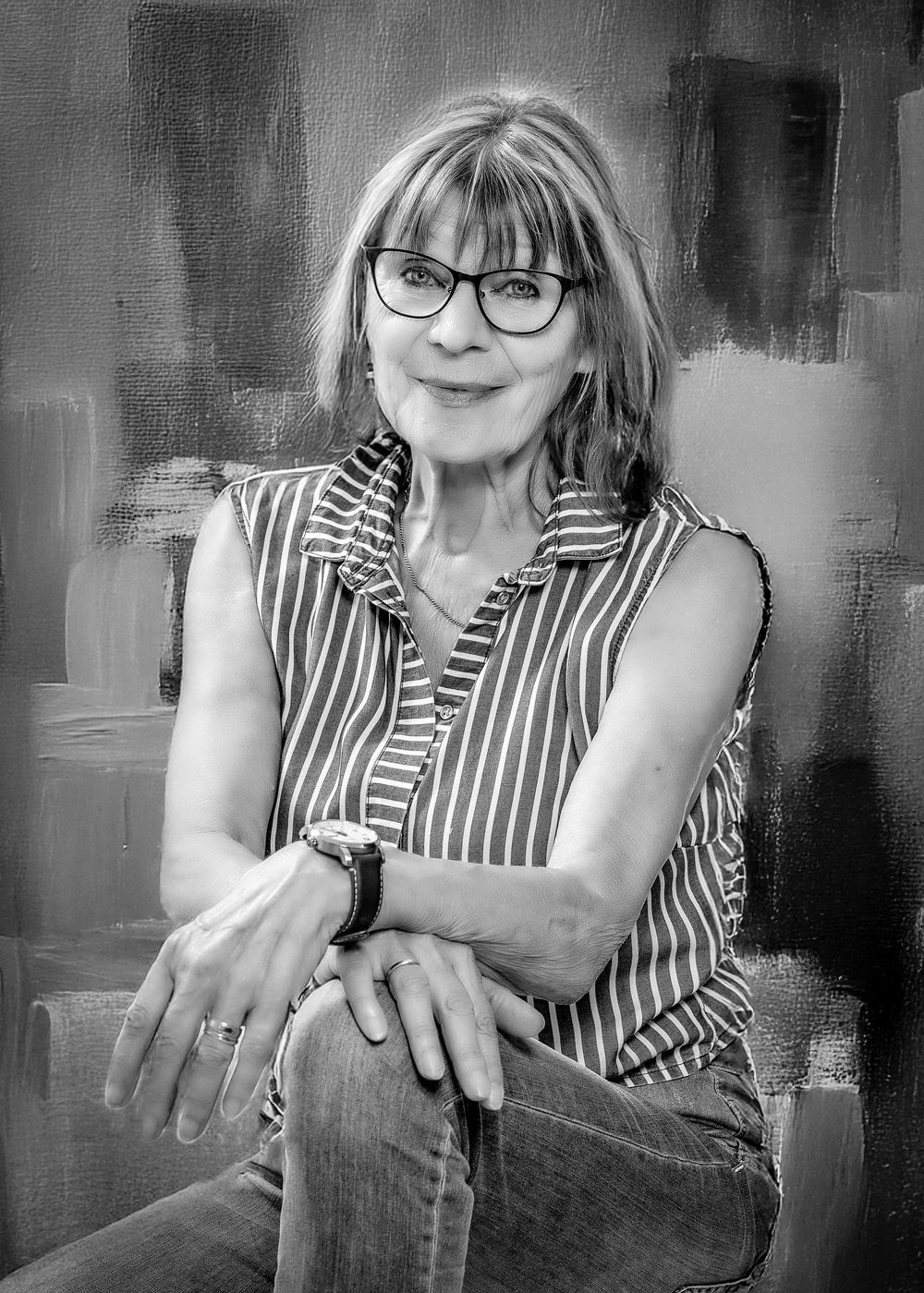 Black and white portrait of someone wearing glasses and a striped sleeveless top against an abstract background.