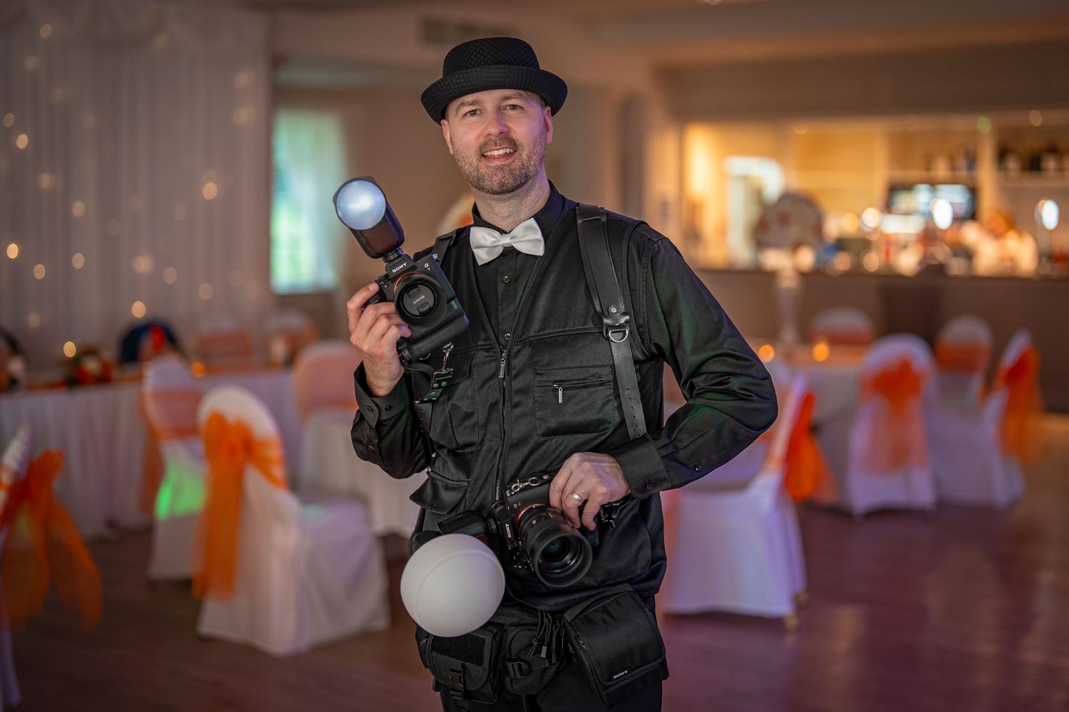 Wedding photographer in formal attire with camera equipment in decorated reception hall.