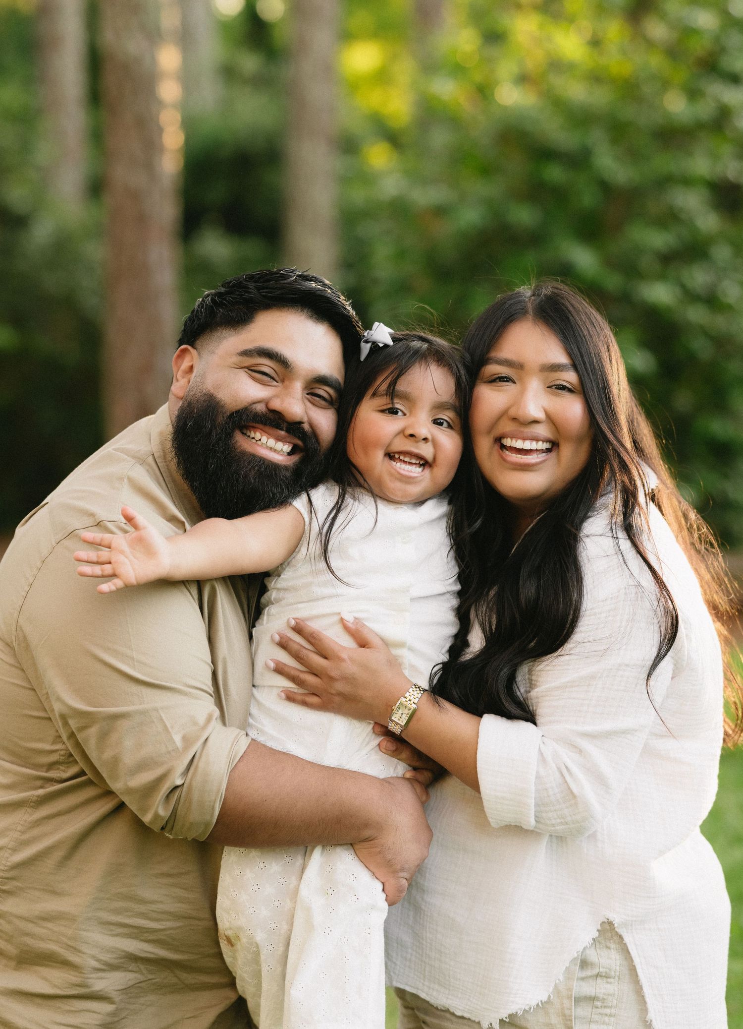 A family of three shares joyful moments in a series of candid photos taken outdoors with natural greenery in background.