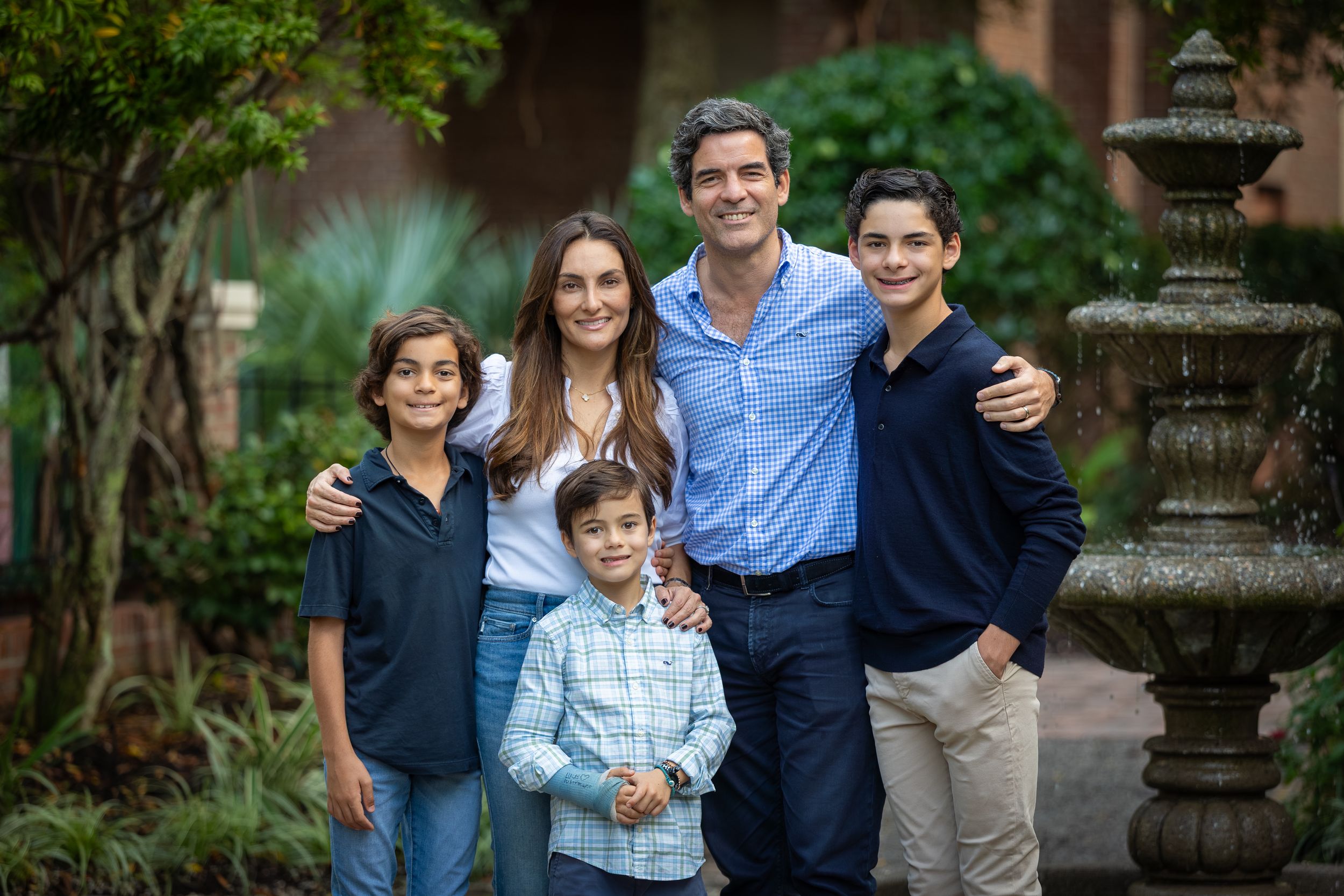 Happy family of five with three boys and parents smiling by a stone fountain in a garden.