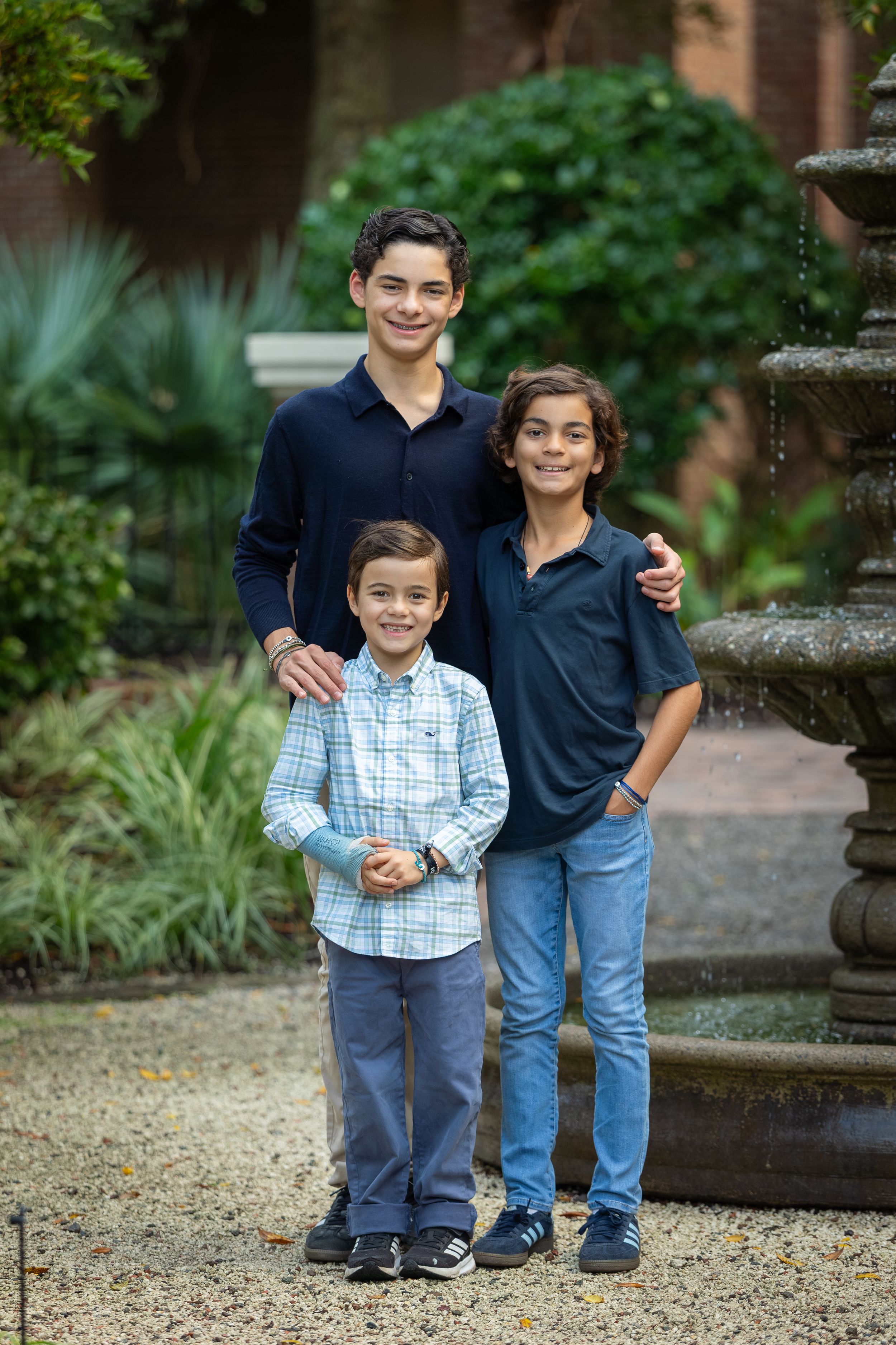 Three brothers posing together by a stone fountain in a lush garden, smiling at the camera.
