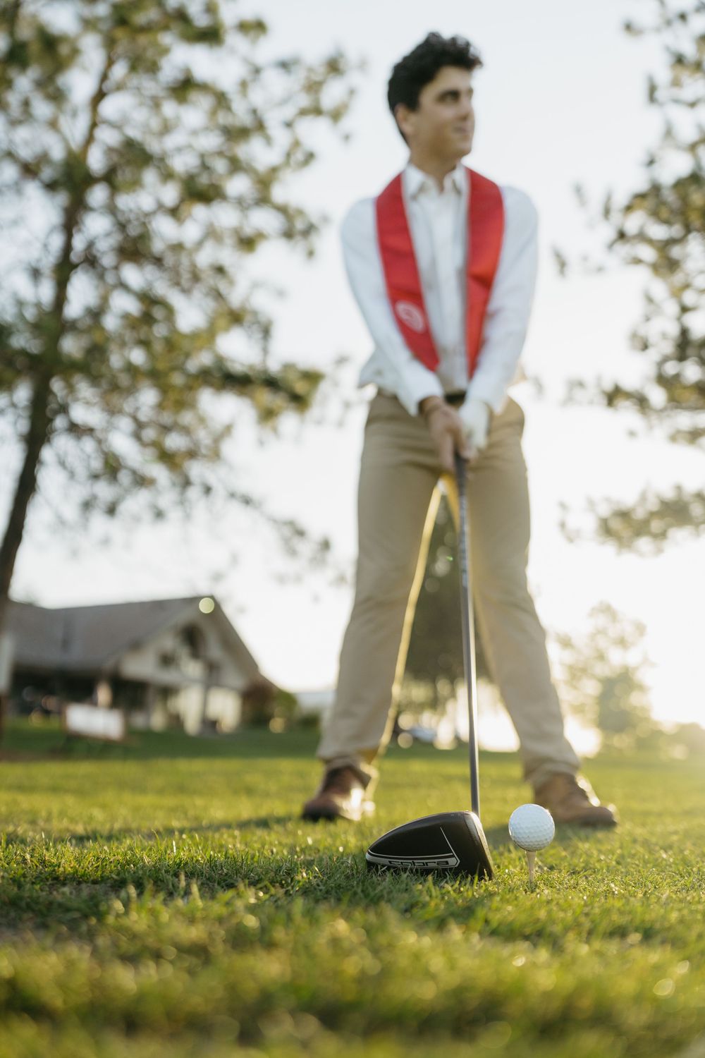 Young man in red vest preparing to tee off with a golf driver on a sunny green course.