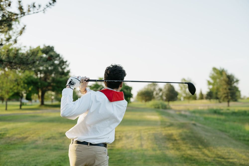 Golfer in white sweater completing a swing follow-through on a lush green golf course on a sunny day.