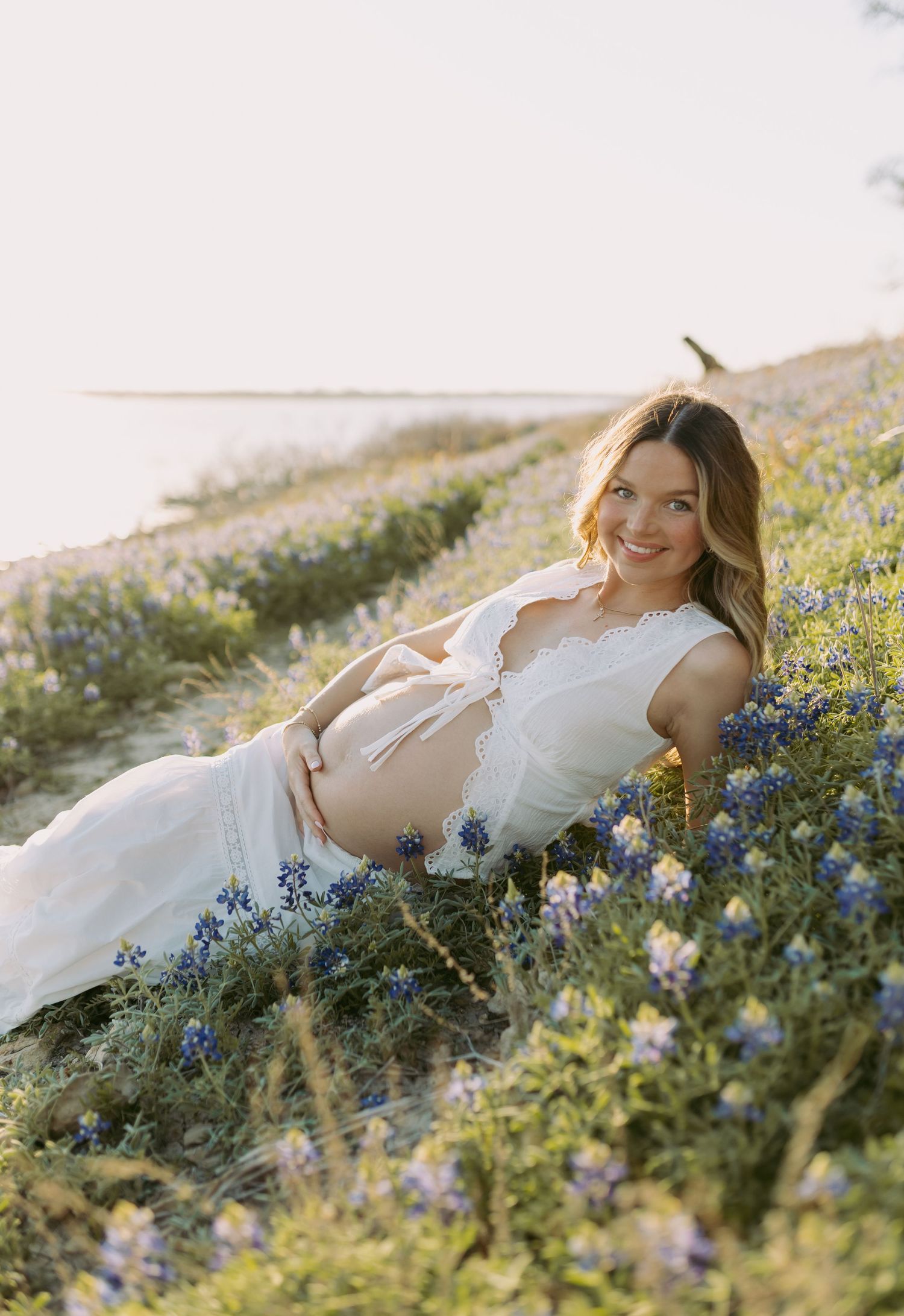 Person in white dress lying in a meadow of blue wildflowers during golden hour sunset.