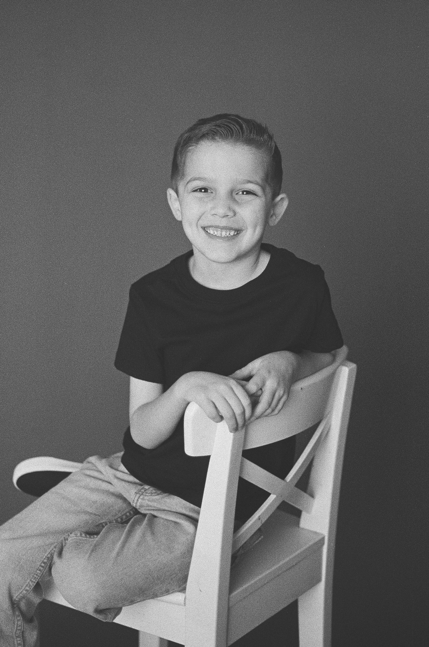Black and white portrait series showing joyful expressions and playful poses in a white chair.