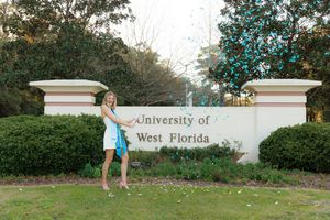 A student poses in front of the University of West Florida entrance sign surrounded by landscaped greenery.