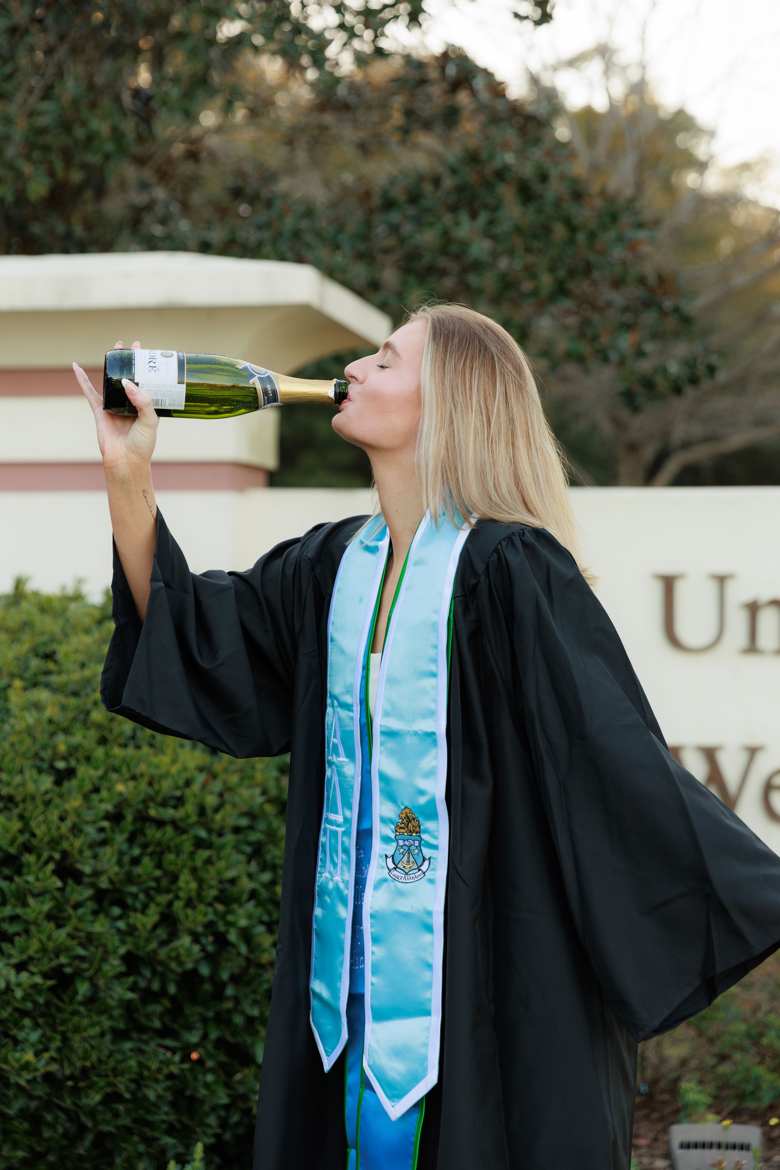 A graduate in black cap and gown with blue sash drinks from a champagne bottle in a celebratory photo series.