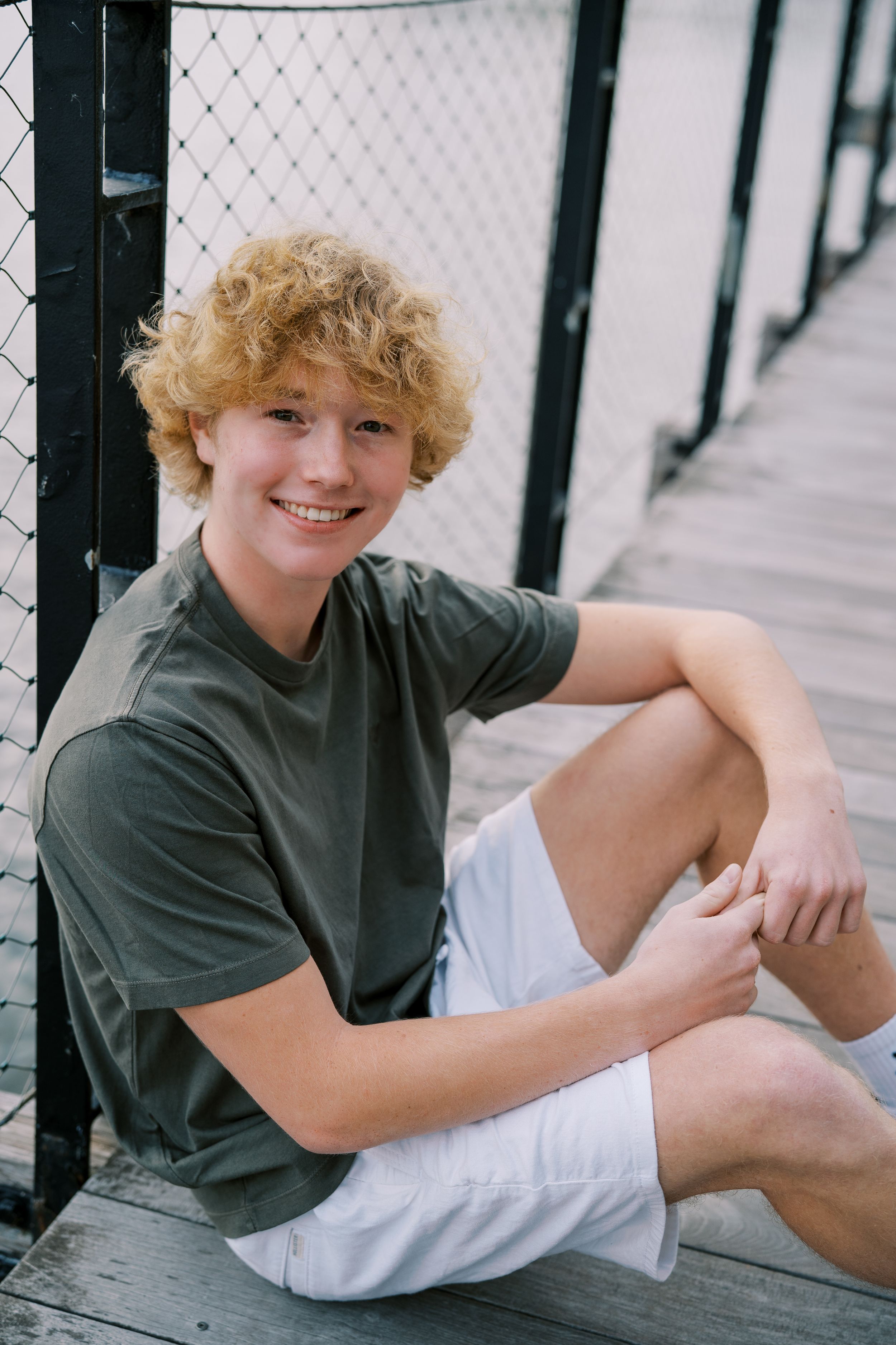 Casual seated portrait on wooden deck wearing green shirt and white shorts.