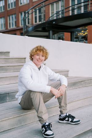 Casual portrait series on concrete steps wearing white sweatshirt and gray pants.